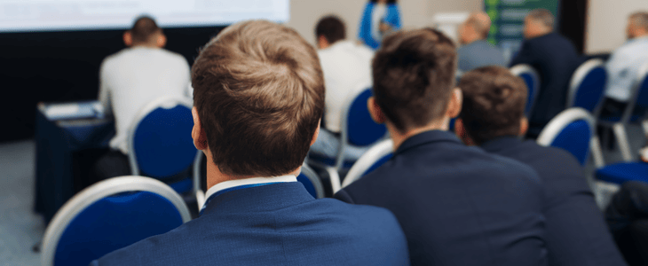 A group of business men sit and listen to a conference presentation